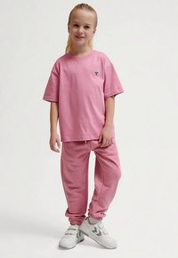 Rosa bomulls-T-shirt med korta ärmar och en hjärtlogga på bröstet, kombinerad med matchande rosa mjukisbyxor med elastiska muddar och dragsko.