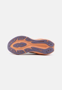 Semelle de chaussure avec base orange et crampons en caoutchouc violet disposés pour la traction sur un fond gris clair.