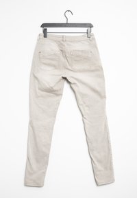 Jeans ajustados beige colgados de una percha negra. Hechos de algodón con dos bolsillos traseros. Textura suave y diseño de pierna recta.