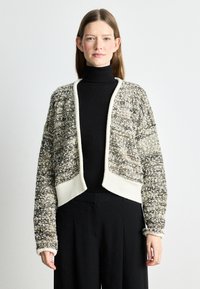 Texturovaný zkrácený kardigan s kombinací bílé, černé a hnědé příze. Má vroubkovaný límec a manžety, otevřený přední design a volný střih.