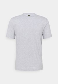 Camiseta gris de manga corta con un cuello redondo, fabricada en una mezcla de algodón. Presenta un pequeño logo verde cerca del cuello.