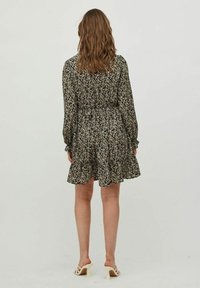 Svart blommig klänning med långa ärmar, smal midja och utsvängd nederkant. Tyget har små vita och gula blommor mot en mörk bakgrund.