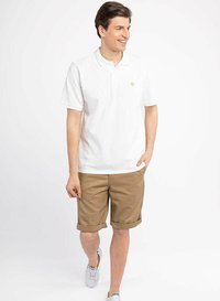 White polo shirt with a collar and short sleeves, paired with beige rolled-up shorts. Shoes are grey sneakers. Smooth fabric texture.