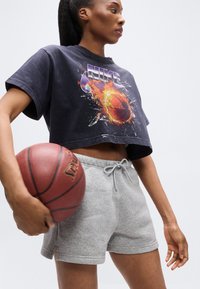 Μαύρο cropped t-shirt με πολύχρωμο γραφικό καλαθοσφαίρισης· γκρι σορτς με κορδόνι· κρατώντας μια κόκκινη μπάλα μπάσκετ· απαλή υφή και άνετη εφαρμογή.