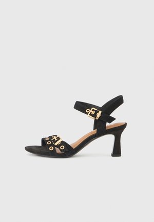 Černá semišová sandála na vysokém podpatku s nastavitelným páskem na kotník, otevřenou špičkou, zlatými kovovými doplňky a strukturovanou podrážkou.