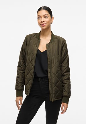 Veste bomber en olive matelassée avec des poignets et un col côtelés, dotée d'une fermeture éclair sur le devant et d'une texture lisse. Portée par-dessus un haut noir.