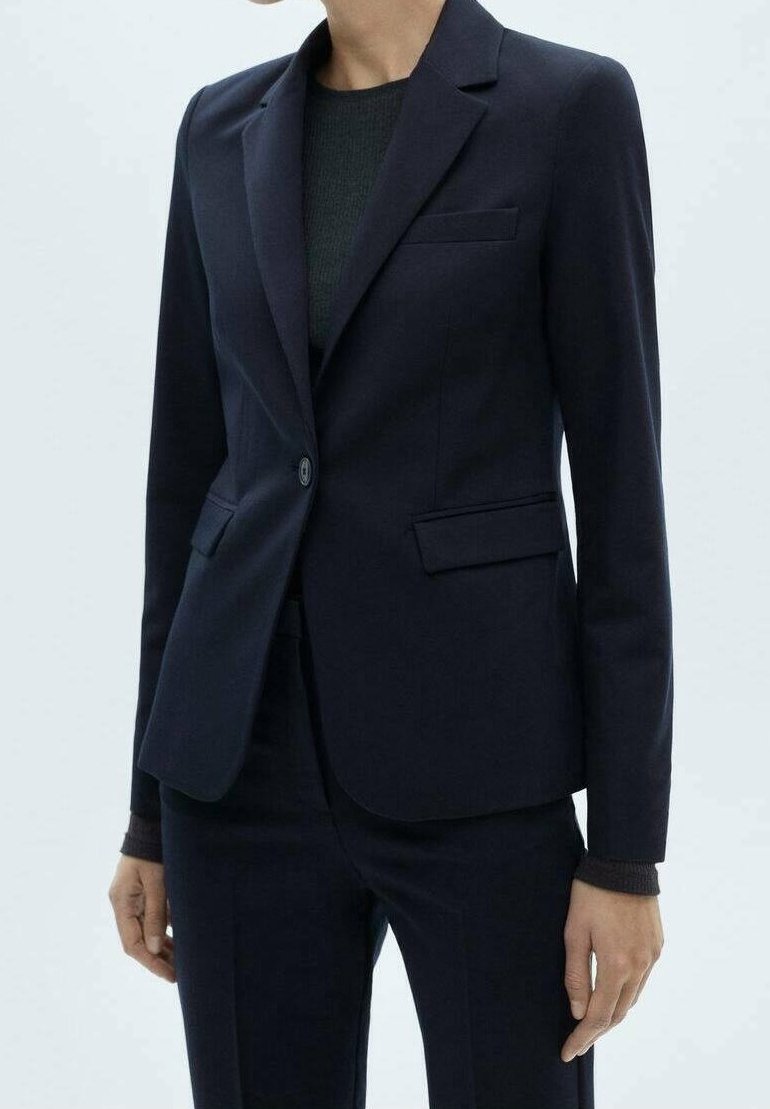 Femme portant un blazer bleu marine foncé cintré avec un seul bouton et un pantalon assorti sur un haut noir.