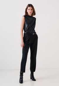 Top nero senza maniche con una texture lucida, abbinato a pantaloni neri a righe sottili e stivali neri con tacco alto. Accessorio semplice a forma di cintura.