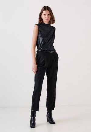 Musta hihaton toppi kiiltävällä pinnalla, yhdistettynä mustiin raitapö trousers ja korkeakorkoisiin mustiin saappaisiin. Yksinkertainen vyövaruste.