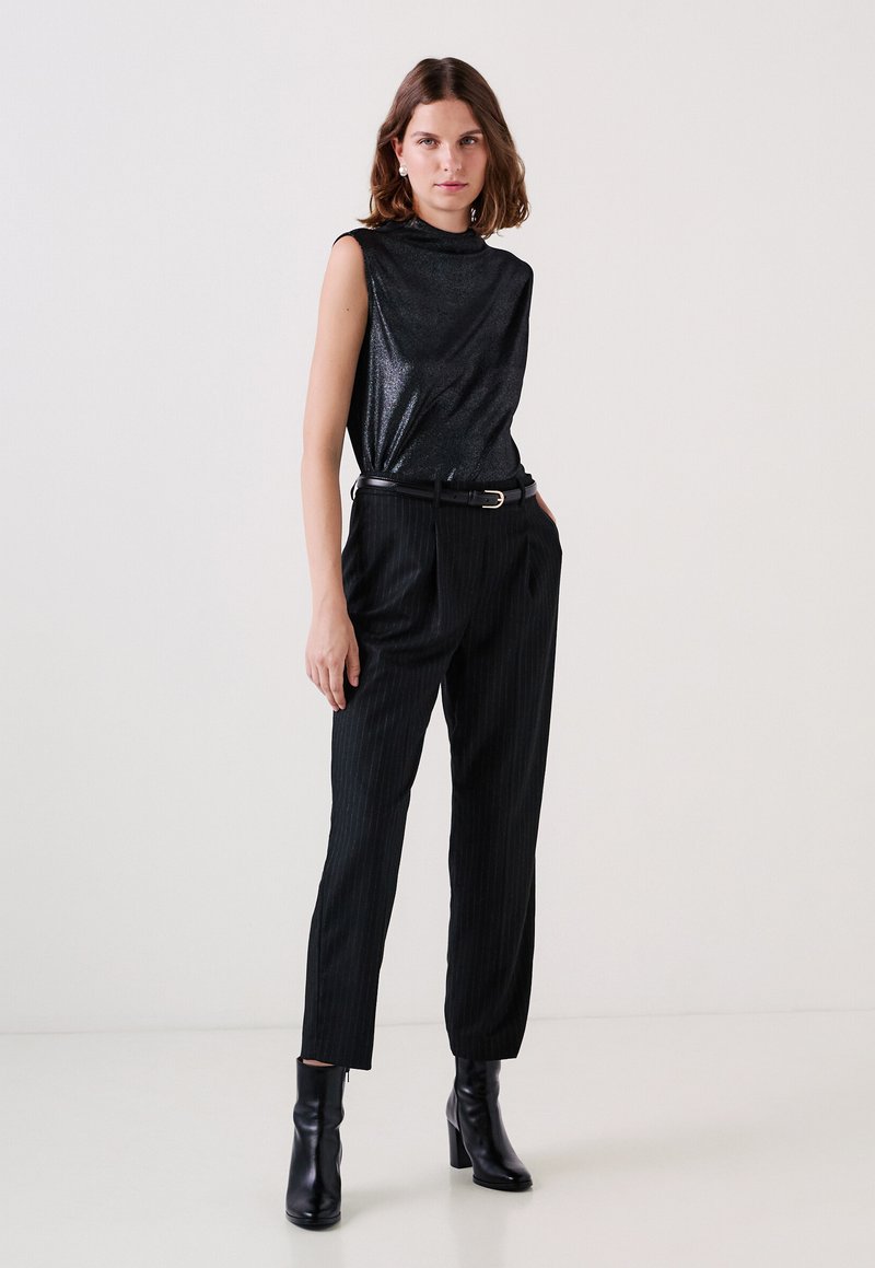 Top nero senza maniche con una texture lucida, abbinato a pantaloni neri a righe sottili e stivali neri con tacco alto. Accessorio semplice a forma di cintura.