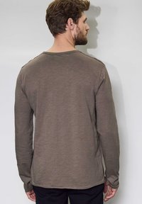 Långärmad skjorta i en dämpad brun färg, tillverkad av mjukt tyg. Den har rundad halsringning och en avslappnad passform, med en rak fåll.