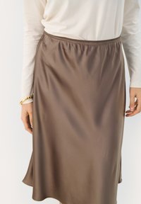 Brun satin midi kjol med elastisk midja. Slät textur, något utsvängd fåll och detaljer med sidsslits. Bärs med en ljus topp.