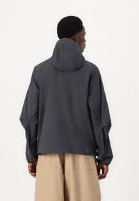 Donkergrijze hooded jack met een ontspannen pasvorm, elastische boorden en een zachte textuur. Heeft een minimalistisch ontwerp en reikt tot heuplengte.