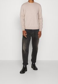 Jasno beżowy sweter z okrągłym dekoltem, zestawiony z ciemnymi dżinsami. Czarne botki za kostkę z masywną podeszwą. Widoczne elementy gładkie i strukturalne.