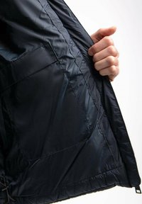Wnętrze czarnej kurtki ocieplanej z gładką, błyszczącą teksturą. Posiada kieszeń boczną i elastyczny dół dla lepszego dopasowania. Ręka umieszczona w środku.