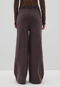 Pantalones de pierna ancha en un tejido marrón oscuro y texturizado, con una cintura elástica y un corte holgado, aptos para un estilo relajado.