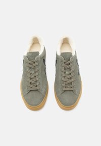 Zöld velúr sportcipők krémszínű gyapjú béléssel, bézs gumi talppal és sötét részletekkel rendelkeznek. Fűzős dizájn, kerek orral.