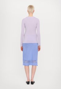 Langshemd lilac top gecombineerd met een blauwe knie-lange rok met een doorschijnende panel bij de zoom. Zwarte platte schoenen maken de outfit compleet.