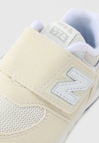 Sneaker beige chiaro in mesh e suede, con una chiusura a strappo bianca e un grande logo "N" bianco sul lato. Modello 574.