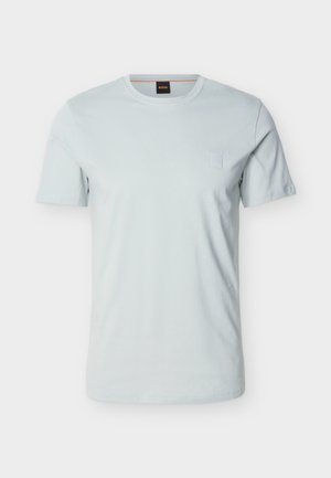 Camiseta azul claro de manga corta con cuello redondo, con un pequeño parche de logotipo tonal en el pecho izquierdo y una etiqueta negra en el interior del cuello.
