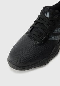 Chaussure de sport noire avec tige texturée, lacets noirs, semelle rembourrée et trois bandes réfléchissantes sur le côté, isolée sur un fond blanc.