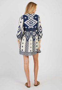 Navyblauw en crèmekleurige jurk met een patroon, ballonmouwen en een taille met een strik, uitgerust met geometrische ontwerpen en een uitlopende rok.