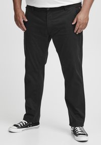 Sorte bomuldsbukser med lige pasform, der har knaplukning, sidelommer og diskrete syninger. Sammen med sorte sneakers.