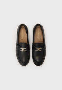 Black leather loafers featuring a gold-tone hardware accent and a cushioned tan insole with perforations for breathability.