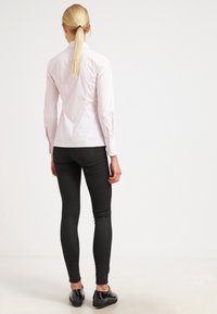 Camicia button-up rosa chiaro con maniche lunghe, abbinata a jeans skinny neri e scarpe nere, vista da dietro.