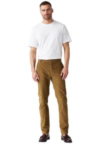 Pantaloni in corduroy beige con taglio dritto, dotati di chiusura con bottone frontale e tasche laterali, abbinati a una maglietta bianca a maniche corte.
