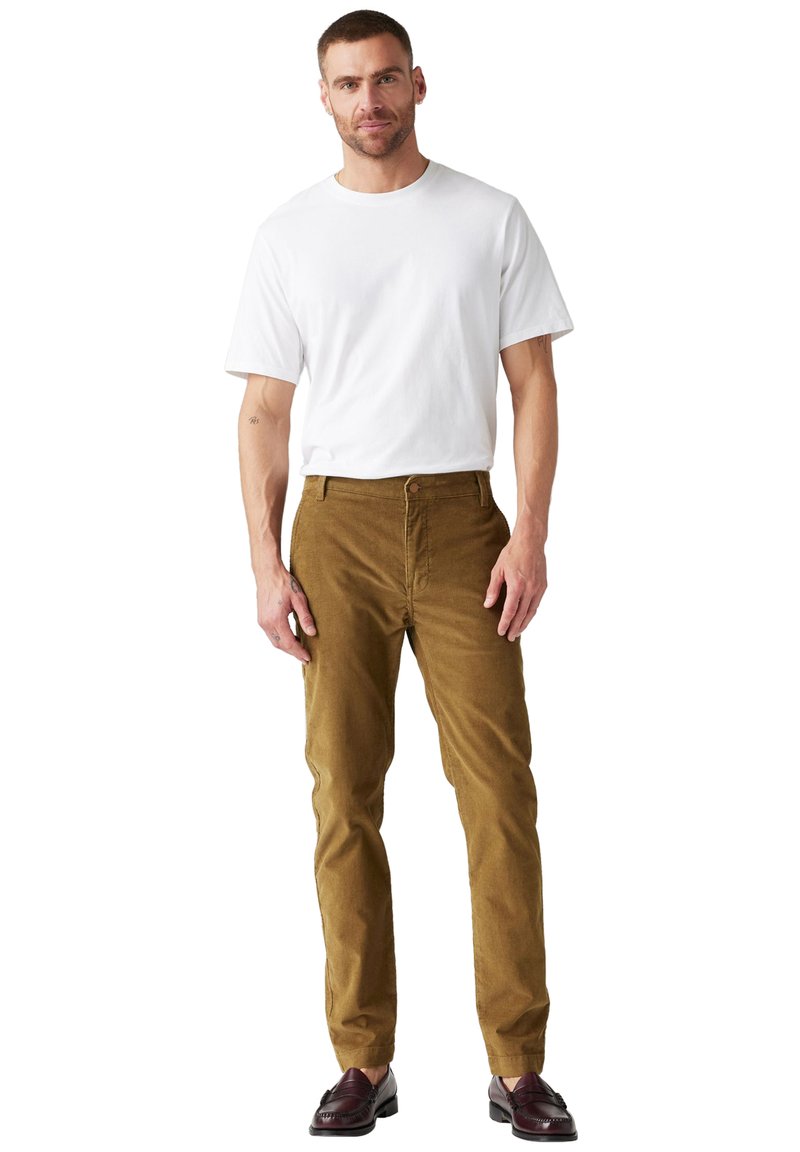 Pantalons en velours côtelé beige à coupe droite, avec une fermeture à bouton à l'avant et des poches latérales, associés à un t-shirt blanc uni à manches courtes.