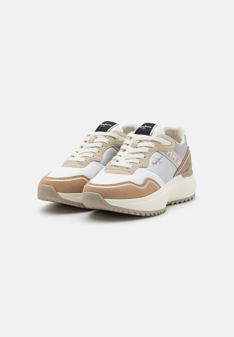Zapatillas deportivas con una combinación de colores en blanco, beige y gris claro. Presentan acentos de ante, suela texturizada y un parche de logo negro en la lengüeta.