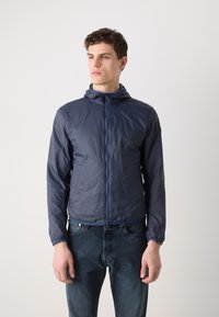 Marineblaue, leichte Jacke mit Kapuze, durchgehendem Reißverschluss, elastischen Bündchen und einer glatten, wasserabweisenden Textur. Kombiniert mit Jeans.
