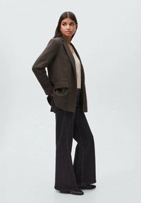 Blazer in lana marrone con vestibilità sartoriale, dotato di due tasche frontali e chiusura a un bottone, abbinato a pantaloni in denim neri a gamba larga.