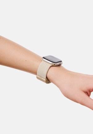 Smartklokke med sølvramme og vevd beige rem, brukt på venstre håndledd mot ensfarget lys bakgrunn.