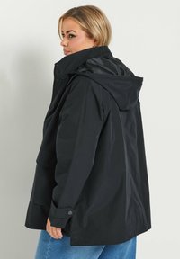 Svart huva jacka med lös passform, med dragkedja framtill, sidofickor och en slät, vattentålig yta.