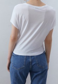 Vit kortärmad T-shirt med avslappnad passform och mjuk textur, i kombination med medelblå högmidjade jeans med en klassisk femficksdesign.