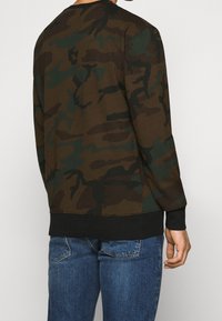 Camo-sweatshirt in bruin- en groentinten, gemaakt van zachte stof, met geribbelde manchetten en zoom. Heeft een ronde hals en een ontspannen pasvorm.