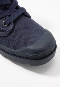 Zapato azul marino con un upper de lona texturizada, punta de goma y suela de goma con patrón; presenta cordones planos y ojetes.