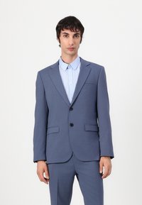 Grau Anzug mit einer Zwei-Knopf-Verschluss, angeschnittenen Revers und vorderen Taschen, kombiniert mit einem hellblauen Hemd mit Knöpfen. Glatte Textur.