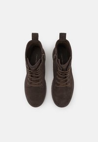 Stivali alla caviglia in suede marrone con lacci, zip laterali e maniglie per il sollevamento, visti dall'alto su uno sfondo bianco.