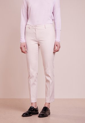 Pantalons ajustés rose clair avec une texture lisse et soyeuse. Associés à des chaussures noires avec des clous en métal et un design à bout arrondi.