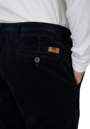 Navy corduroy pants with a textured surface, featuring a back pocket with a brown leather label and a contrasting button.