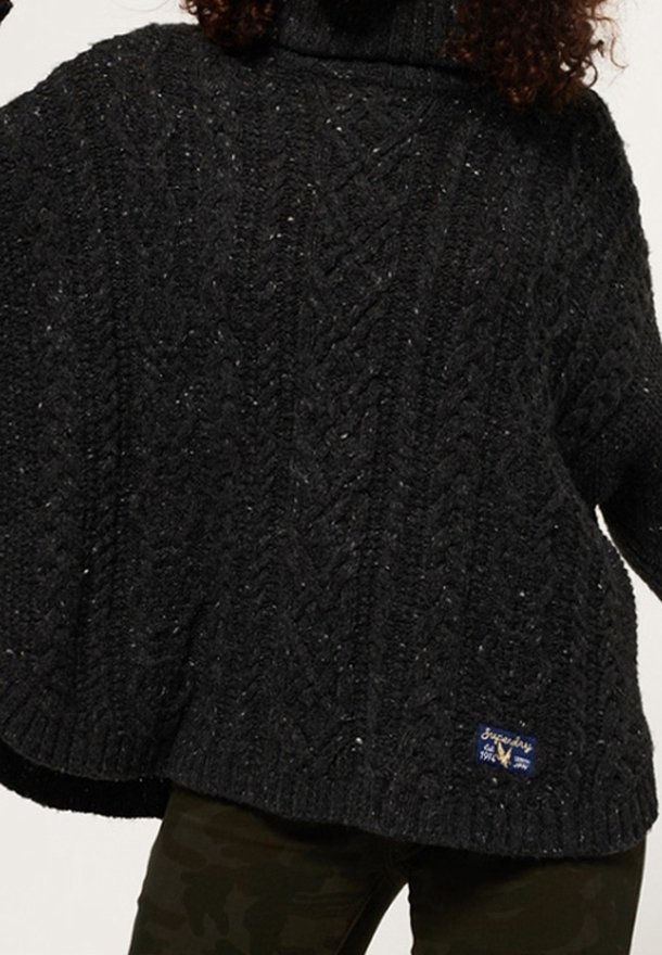 Zwarte chunky gebreide coltrui met kabelpatronen, gedragen over donkere camouflagebroek.