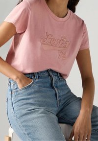 T-shirt en coton rose clair avec logo en relief "Levi's 73", associé à un jean en denim bleu taille haute avec des bords de poches effilochés.