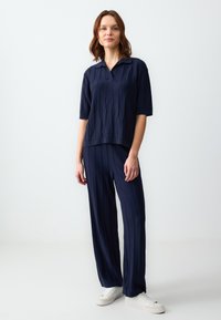 Navy gestricktes Zweiteiler-Set mit einem kurzärmeligen Poloshirt mit strukturiertem Muster und weit geschnittenen Hosen, beide mit vertikalen Streifen.