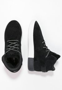 Baskets montantes en daim noir avec une tige texturée, semelle en caoutchouc blanc contrastant et lacets noirs à motifs. Comprend un col rembourré et un logo.