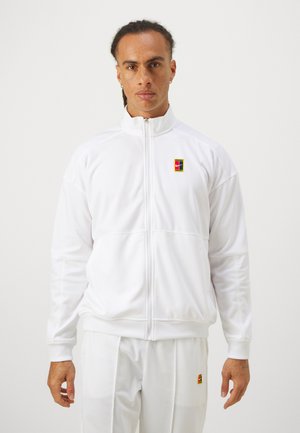 Weiße sportliche Jacke mit Reißverschluss, hohem Kragen, elastischen Manschetten und Saum. Mit einem mehrfarbigen Logo auf der linken Brust und glattem Stoff.