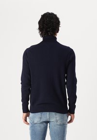 Mörkblå, långärmad stickad tröja med hög krage. Har ribbade mudd och avslut, slät textur och en figurnära design.