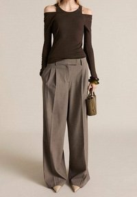 Haut marron à épaules dénudées et manches longues associé à un pantalon large à taille haute plissé gris et des chaussures à bout pointu beiges. Petit sac à main inclus.